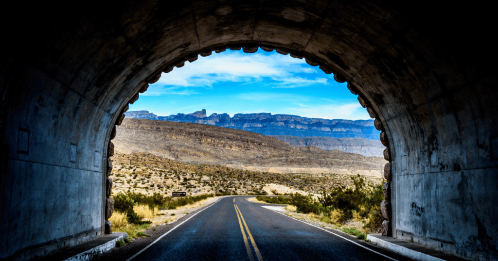 Tunnel exit with a clear view of the road leading outside and a bright sky.