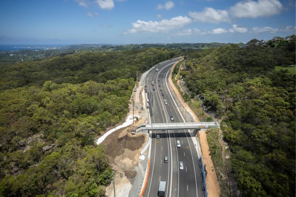 Aerial view of the completed Mona Vale Road East Upgrade showing widened lanes, a new bridge and smooth traffic flow through a bushland corridor.