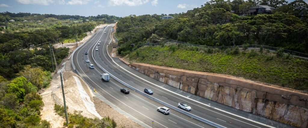 Aerial view of the completed Mona Vale Road East Upgrade showing widened lanes, smooth traffic flow and rock cuttings through the surrounding bushland.