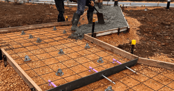 Workers pouring concrete over rebar supported by Combination SOG Bar Chairs Cliptop on a slab-on-ground site.
