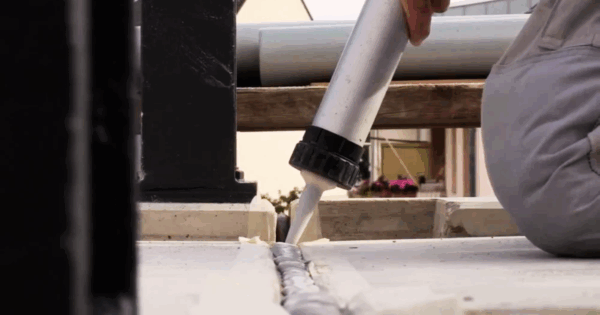 Applying polyurethane joint sealant with caulking gun for expansion joint sealing in concrete.