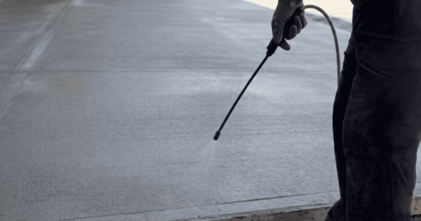 Worker applying concrete curing compound to a freshly finished concrete slab using a spray applicator for effective moisture retention.