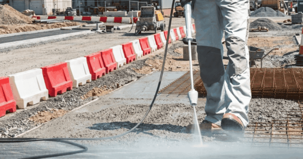 Worker using a curing compound spray to apply a concrete curing agent on a newly poured concrete surface.